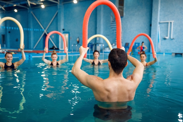 Instrutor masculino e grupo feminino, treinamento de hidroginástica na piscina