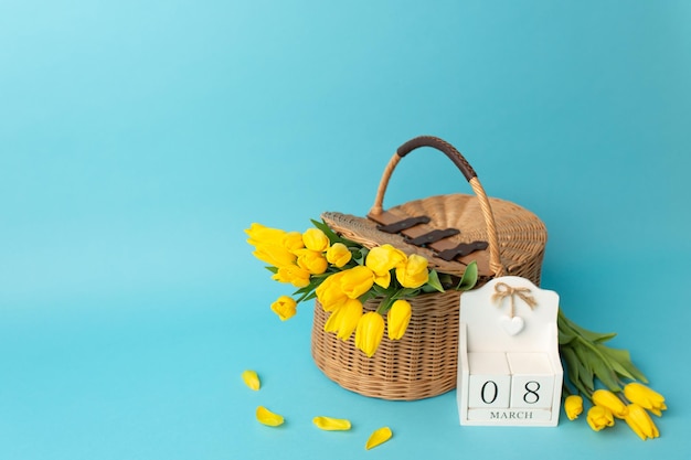 Intarnationaler Frauentag Holzkalender 8. März und gelbe Tulpen in einem Korb mit Reben auf blauem Hintergrund Kopierbereich