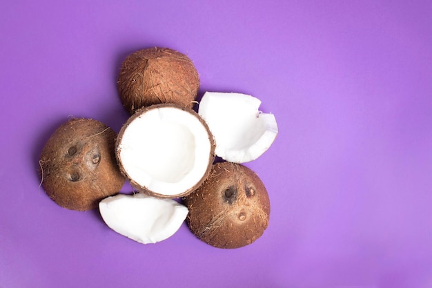 Inteiro e metades de cocos e fatias isoladas em fundo roxo, vista superior. cocos