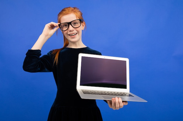 Inteligente chica adolescente pelirroja con gafas tiene un portátil con una pantalla en blanco