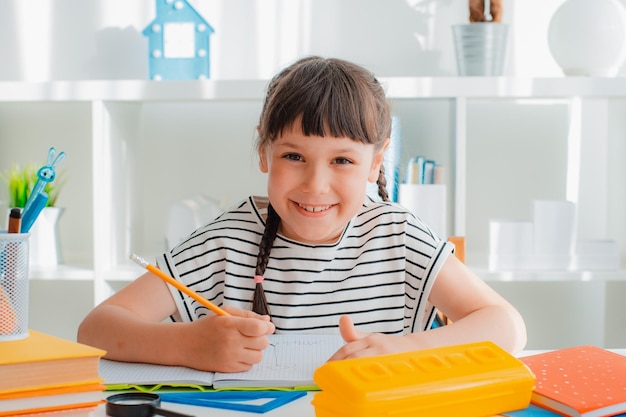 Inteligente e concentrada pequena menina caucasiana de 7 anos sentada mesa de estudo em casa distante fazer lição de casa com livros didáticos