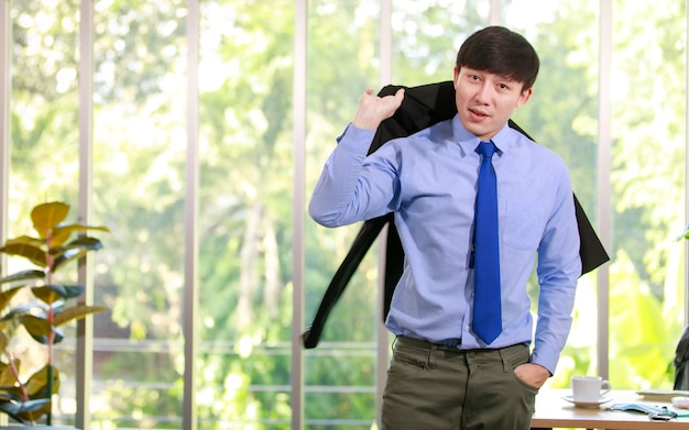 Inteligente jovem empresário executivo em terno de trabalho formal e gravata elegante em pé com confiança no escritório da empresa e carregando jaqueta pronta para desfrutar do estilo de vida da gestão corporativa no verão
