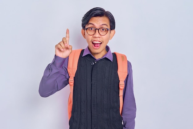 Inteligente jovem estudante asiático de 20 anos vestindo roupas casuais com mochila apontando o dedo para cima com uma ótima nova ideia isolada em fundo cinza Conceito de faculdade universitária de ensino médio