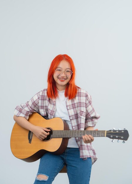 Intelligente asiatische Frau mit roten Haaren und Brille Musiker spielt Gitarre auf grau oder weißem Hintergrund Gitarrist Musikkonzept Asien Frauen mit akustischer Gitarre schauen in die Kamera im Studio Beleuchtung