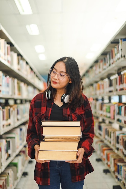 Intelligente asiatische Studentin im lässigen Stil bringt einen Stapel Bücher in die Bibliothek