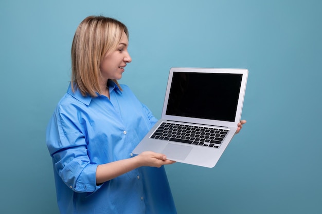 Intelligente, aufmerksame junge Frau in einem Freizeithemd, die einen Laptop mit einem Mockup in ihren Händen auf einem Blau hält