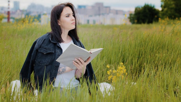 Intelligente kaukasische Frau sitzt auf Rasen im Freien und liest Buchliteratur-Psychologie-Bestseller