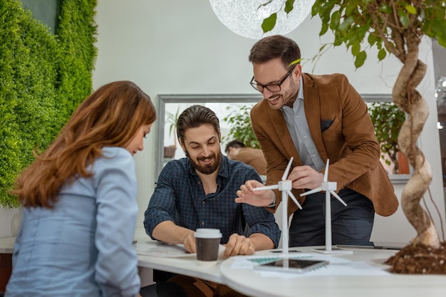 Intelligente, qualifizierte, qualifizierte junge Ingenieure, die das Projekt der alternativen Energie mit Miniaturen von Windmühlenturbinen am Tisch betrachten.