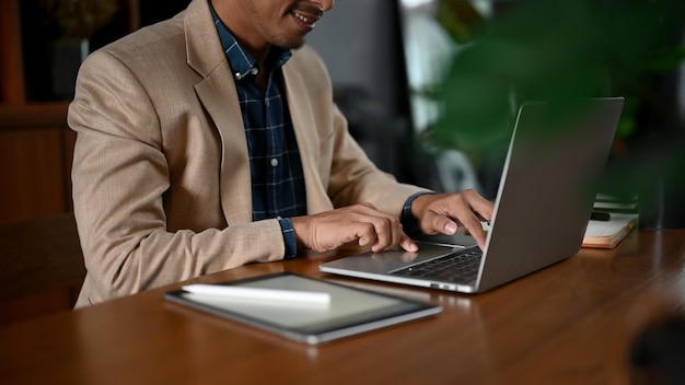 Intelligenter erwachsener asiatischer Geschäftsmann, der seinen Laptop-Computer an ihrem Schreibtisch verwendet