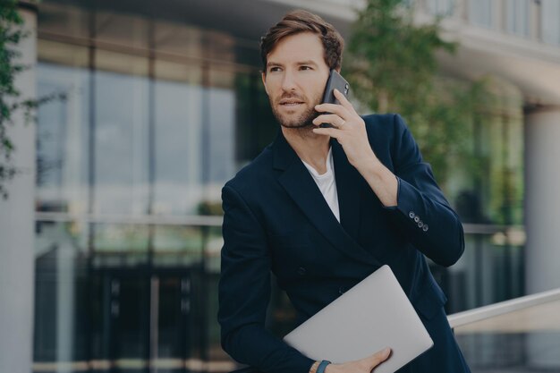 Intelligenter Geschäftsmann spricht beim Gang zum Büro am Telefon