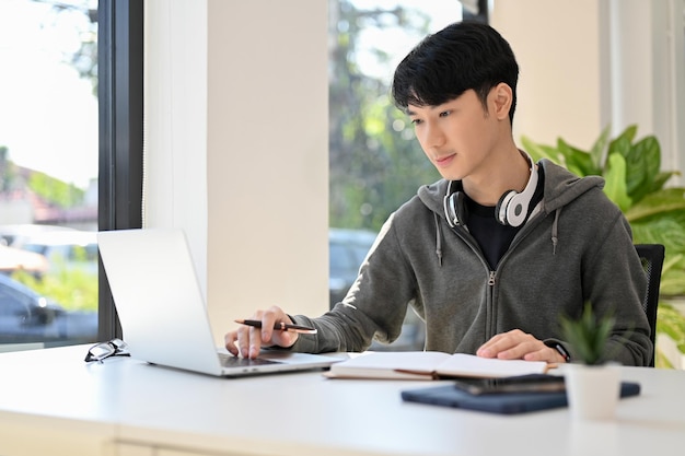 Intelligenter junger asiatischer männlicher College-Student, der seine Schulhausaufgaben macht