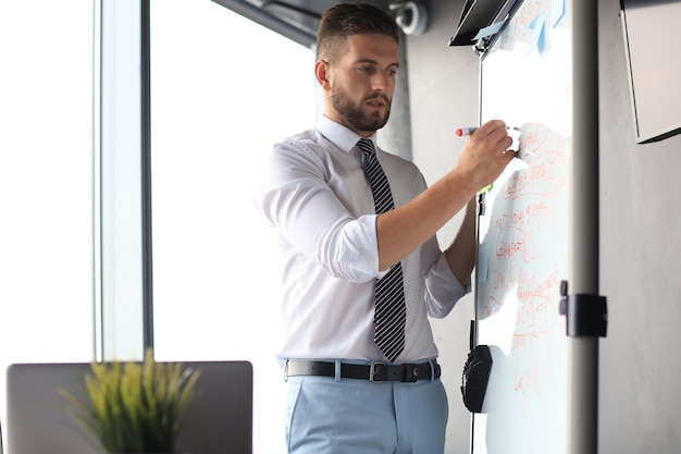 Intelligenter konzentrierter Geschäftsmann, der mit Marker etwas auf das Flipchart schreibt.