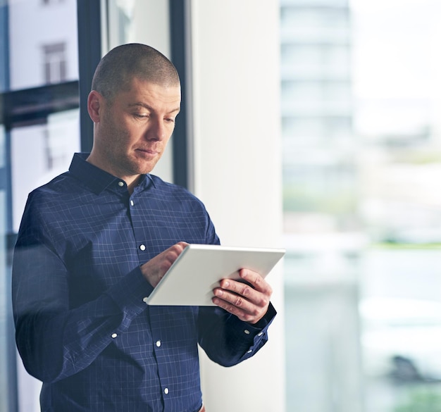 Intelligentere Geschäftsforschung unterstützt durch intelligente Technologie Aufnahme eines Geschäftsmanns, der ein digitales Tablet in einem modernen Büro verwendet