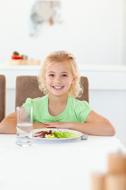 Intelligentes Mädchen, das an einem Tisch sitzt, um ihren gesunden Salat zu essen