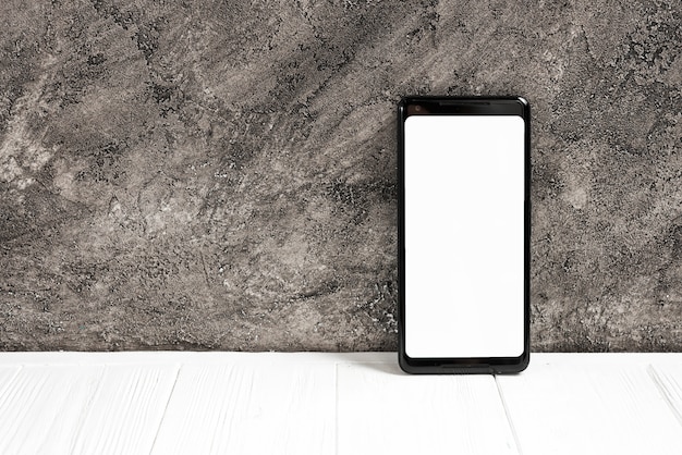 Intelligentes Telefon mit weißem Bildschirm auf weißer Tabelle gegen Betonmauer