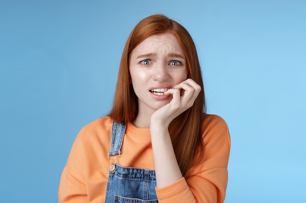 Intensa preocupação assustada jovem ruiva insegura em pânico garota boba carrancuda olhando chateada ansiosa roer unhas emocional assustado despedido em pé fundo azul emocional apavorado