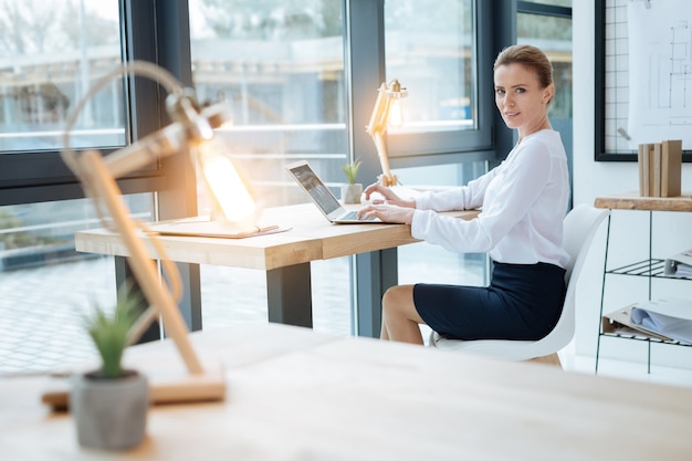 Intensiv arbeiten. Zuversichtlicher Manager, der einen Laptop benutzt, während er Sie ansieht und Vertrauen ausdrückt