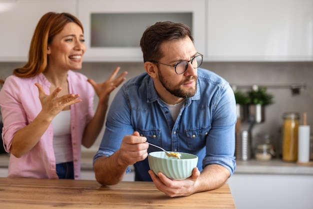 Intenso desentendimento entre um casal em sua cozinha o homem levanta a mão de forma defensiva ambos exibem fortes emoções refletindo um momento desafiador em seu relacionamento