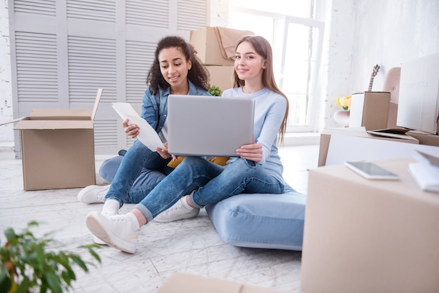 Intercambio de ideas. Hermosas chicas jóvenes sentadas en el suelo y discutiendo ideas sobre la decoración de la pared, mirando a través de las tablas de colores