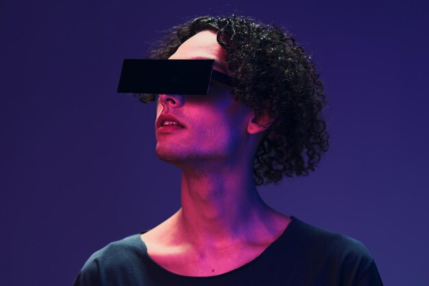 Foto interesado hombre rizado curtido con estilo en camiseta negra gafas de moda posando aislado en color rosa azul fondo de estudio oferta de moda fresca concepto de nueva colección de realidad virtual espacio de copia para anuncio