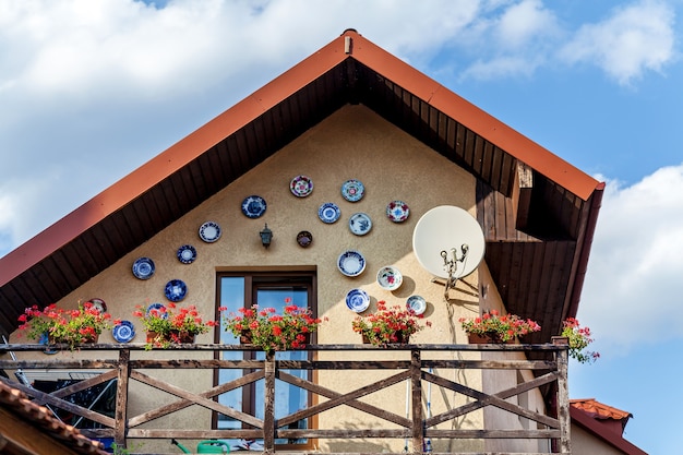 El interesante exterior de una casa con macetas de barro para flores contra un cielo azul. La pared está decorada con platos de cerámica.