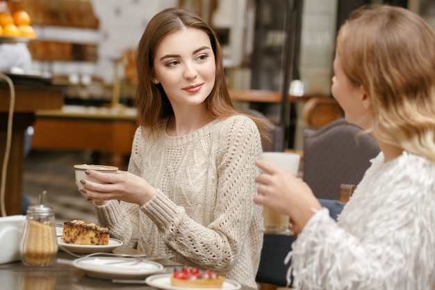 Interessant. Horizontales Porträt einer schönen lächelnden Brünettenfrau, die eine Tasse Kaffee auf ihren Freund hört