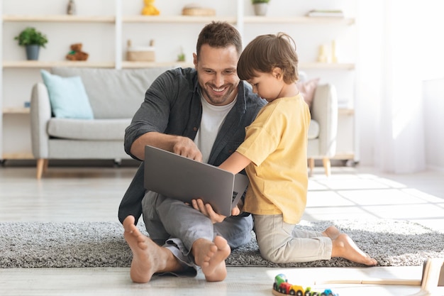 Interesses de crianças modernas Menino bonitinho assistindo seu pai trabalhando no laptop homem alegre mostrando ao filho como trabalhar on-line