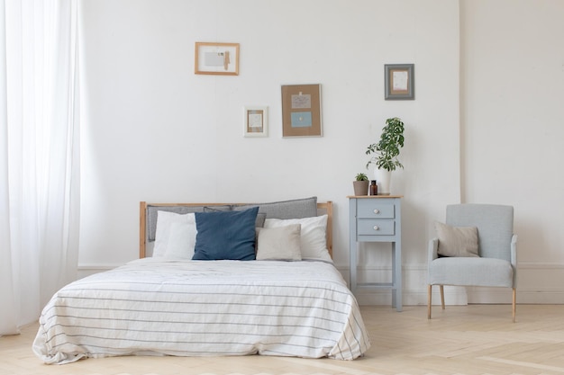 Interior del acogedor dormitorio blanco y gris con plantas en la mesita de noche