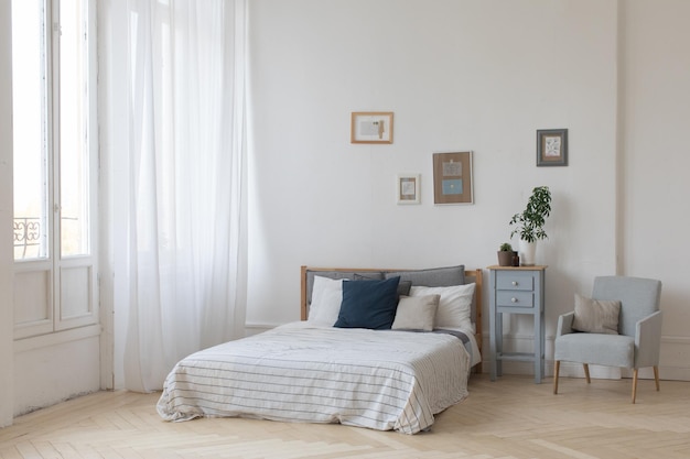 Interior del acogedor dormitorio blanco y gris con plantas en la mesita de noche