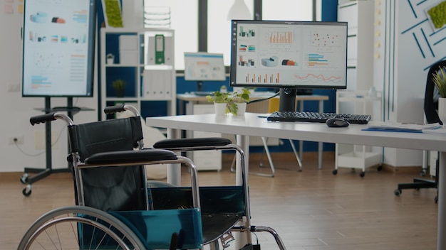 Interior de la acogedora sala de empresa de luz con silla de ruedas estacionada cerca del escritorio