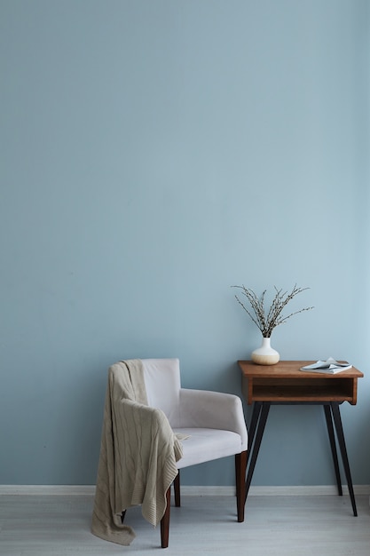 Interior acolhedor da mesa de madeira vintage poltrona retrô com revista e vaso nele no fundo da parede azul e piso de madeira.