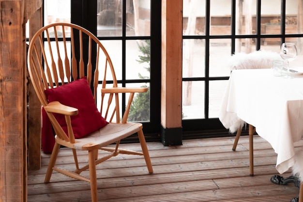 Interior acolhedor do restaurante de madeira. Uma cadeira com uma almofada de sofá e uma mesa junto à janela com talheres