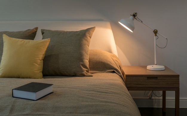 Foto interior acolhedor quarto com livro e lâmpada de leitura na mesa de cabeceira