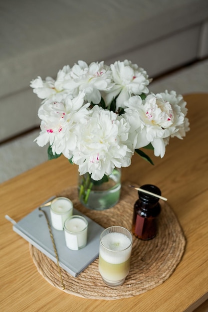 Foto interior aconchegante em casa velas um buquê de peônias em um vaso de vidro um copo de matchalate em uma mesa de centro de madeira primavera