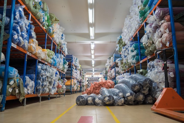 Foto interior de un almacén industrial con muchos estantes con rollos de tela de colores el trabajador levanta la tela del rollo y verifica la cantidad