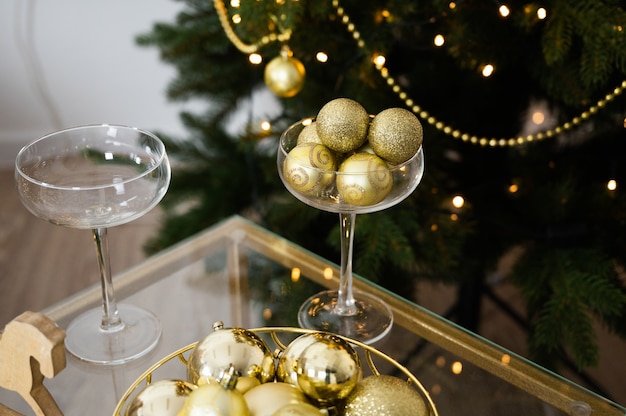 Interior de año nuevo con árbol de Navidad en el fondo. Mesa de Nochevieja o Navidad, copas de cava y bolas doradas.