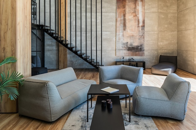 Interior del apartamento de soltero joven en estilo loft con muebles blandos en primer plano, escalera de metal y armario en el fondo