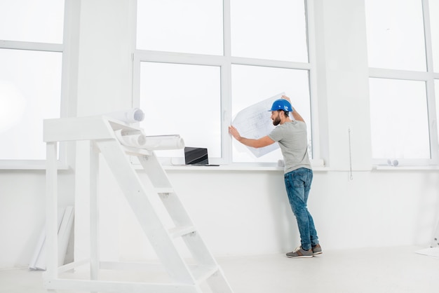 Interior blanco para renovación y reparación con escalera, ventanas y capataz o constructor mirando dibujos en papel