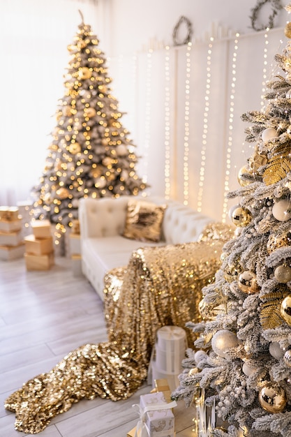 Interior branco de ano novo moderno com duas árvores de natal decoradas com tecidos dourados e presentes dourados