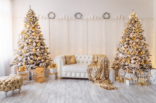 Interior branco de natal moderno com árvores de ano novo decoradas com pufes de ouro e presentes têxteis