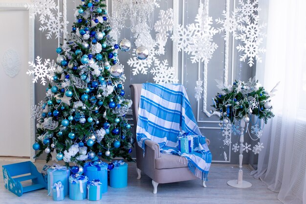 Interior de la casa de año nuevo en azul con un árbol de Navidad, una silla y copos de nieve