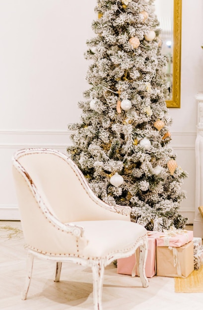 Interior clássico de um quarto branco com uma árvore de Natal, guirlandas, lanternas, presentes e poltrona branca. foto