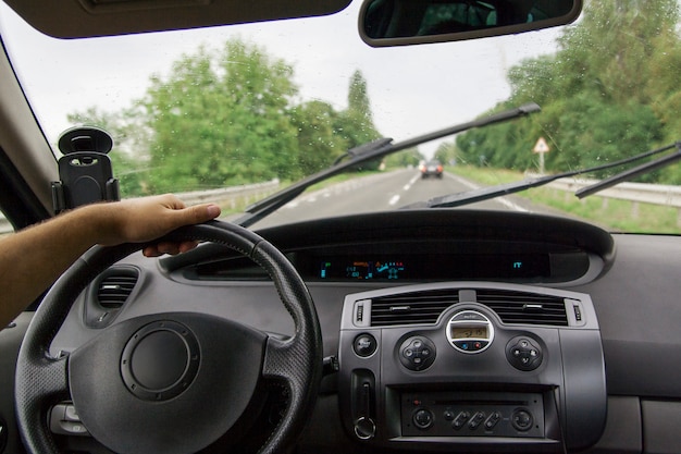 Interior del coche con la mano del conductor en la pista en el verano. Turismo automovilístico, viaje en auto concepto