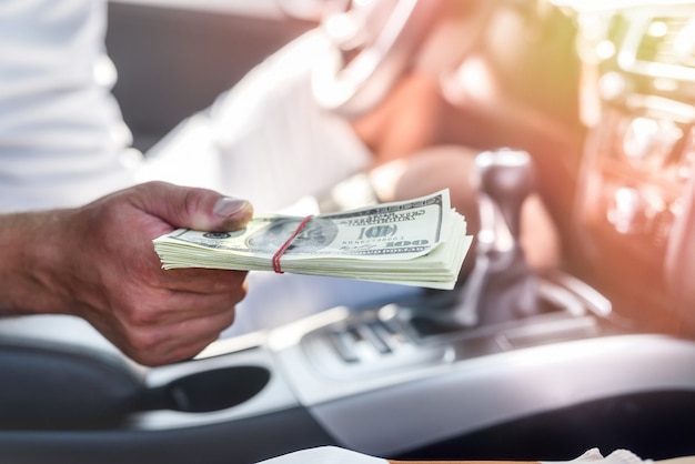 Interior del coche con mano masculina sosteniendo un paquete de dólares de cerca. Imagen tonificada