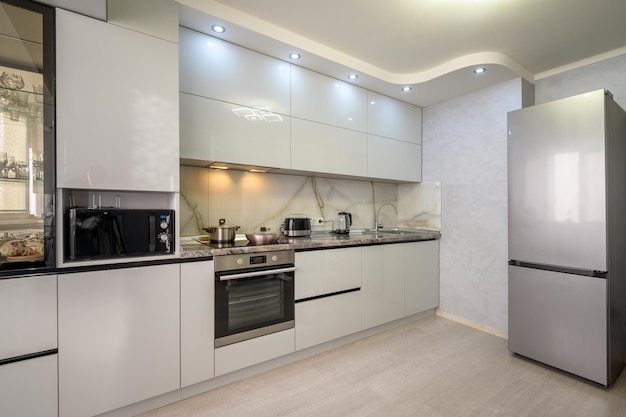 Cocina con muebles de madera gris combinados con encimera de piedra blanca  y armarios de pequeños electrodomésticos vitrocerámica y horno microondas  junto a la puerta de entrada a un apartamento de alquiler