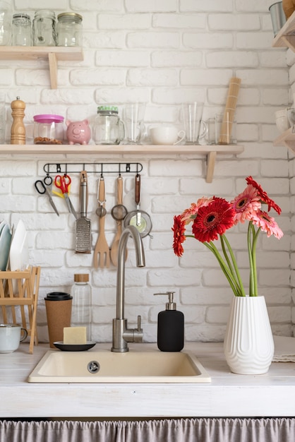 Foto interior de cocina blanca rústica con flores rojas de gerbera fresca en un jarrón blanco