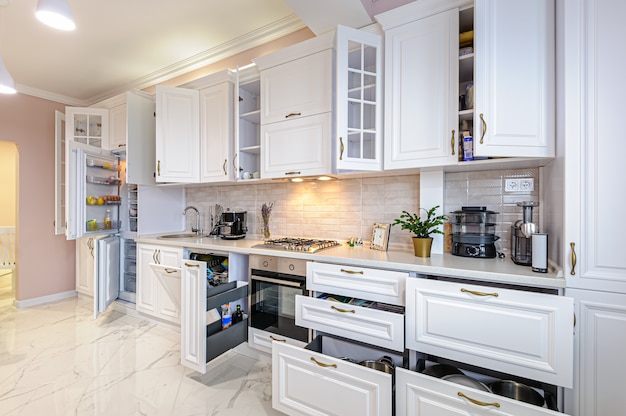 Interior de cocina blanco moderno con puertas y cajones abiertos.