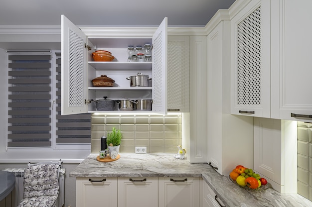 Interior de cocina clásica contemporánea blanca acogedora y cómoda con muebles de madera, el gabinete está abierto, utensilios de cocina en los estantes