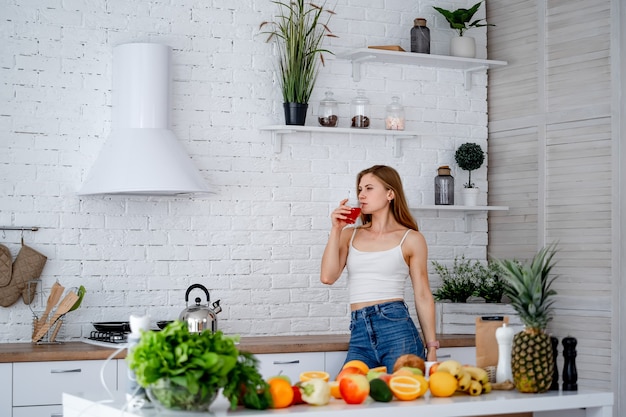 Interior de cocina moderna. Concepto de dieta. Retrato de una mujer joven sana con figura agradable cerca de la mesa con frutas y verduras en la cocina, concepto de comida sana.