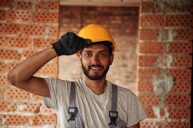 En el interior contra la pared de ladrillo Un guapo hombre indio está en el sitio de construcción